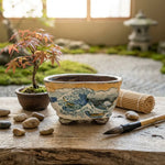 Pot de Tosui décoré, posé sur une table en bois avec pinceau, pierres et petit bonsaï; ambiance zen japonisante.